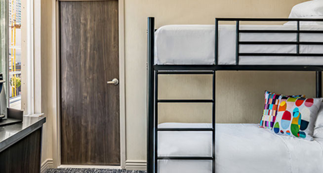 King Bed with Bunk Beds for 2 view showing bunk beds with colorful throw pillows, and large window for viewing city.