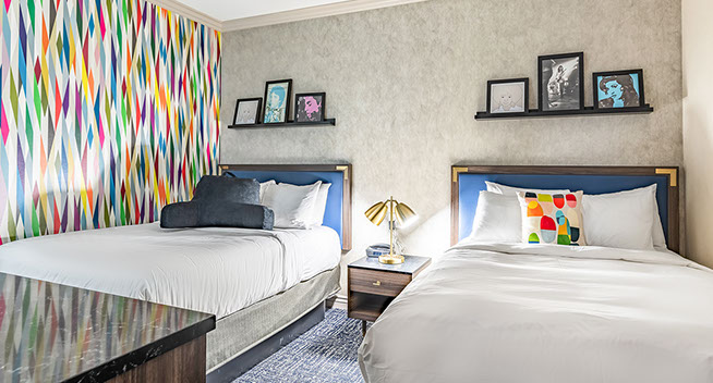 2 Full size beds View of room showing to full size beds with  a trendy style decorated room with colorful wall paper and pillows. Night stand and lamp.