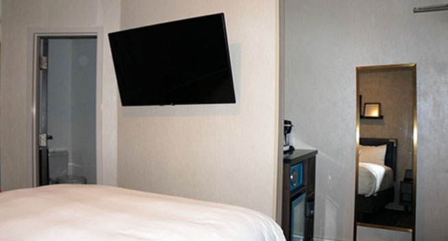 Full Size Guest Room Full size bed, flat screen television with safe for valuables. Mirror at foot of bed. Bathroom entrance to the left of the bed.