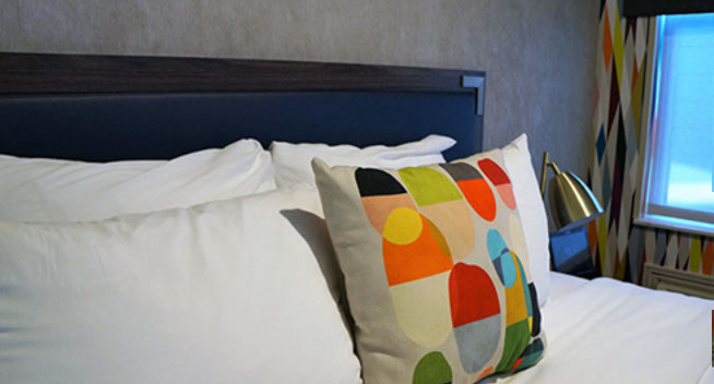 2 Full Beds guest room Close up of Full size bed, colorful throw pillow and large window looking out over city of San Francisco.