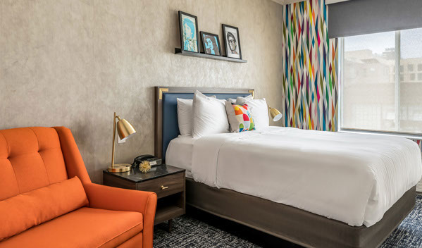 Standard Queenn Bed This is our Queen room with a metro modern ambiance, with colorful and trendy decor. Photo showing Queen bed with night stand and orange chair.